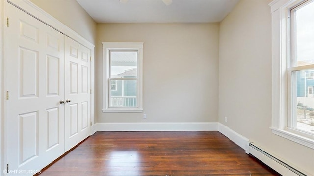 unfurnished bedroom featuring multiple windows, a baseboard heating unit, and a closet