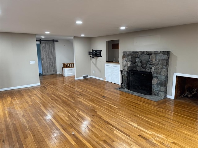 unfurnished living room featuring a barn door, a fireplace, visible vents, baseboards, and hardwood / wood-style floors