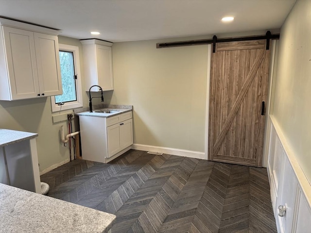 washroom with a barn door, recessed lighting, a sink, and baseboards