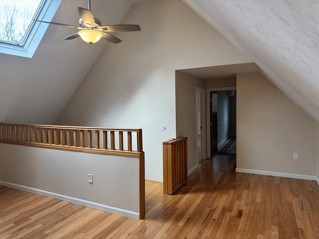 additional living space with light wood finished floors, baseboards, lofted ceiling with skylight, and a ceiling fan