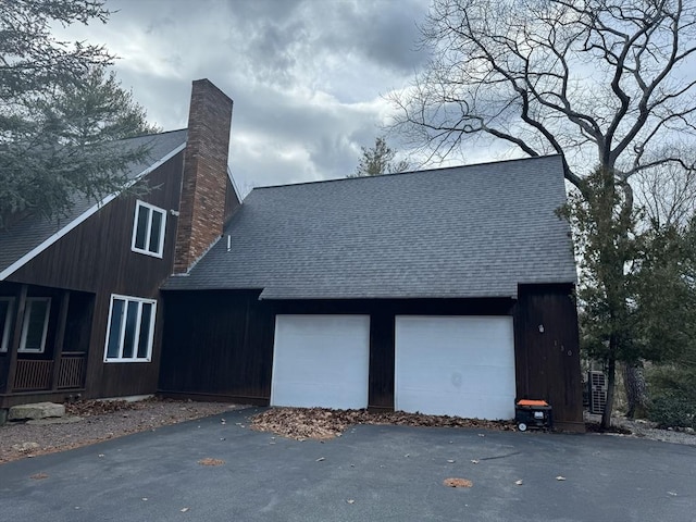 view of property exterior with a shingled roof, driveway, and a chimney