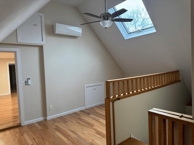 bonus room featuring a skylight, baseboards, a ceiling fan, a wall unit AC, and light wood-style flooring