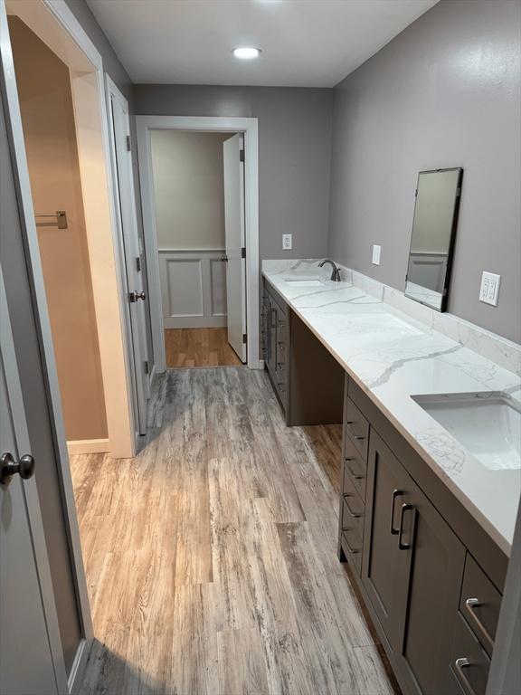 bathroom with double vanity, a decorative wall, a sink, and wood finished floors