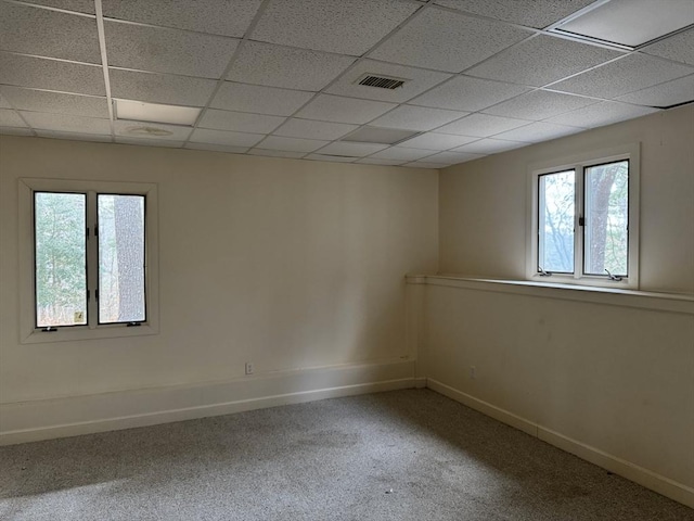 carpeted spare room featuring a drop ceiling, plenty of natural light, and baseboards