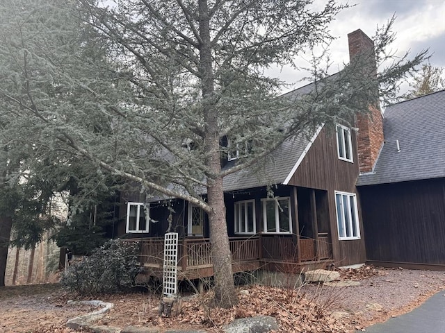 exterior space with covered porch, a shingled roof, and a chimney