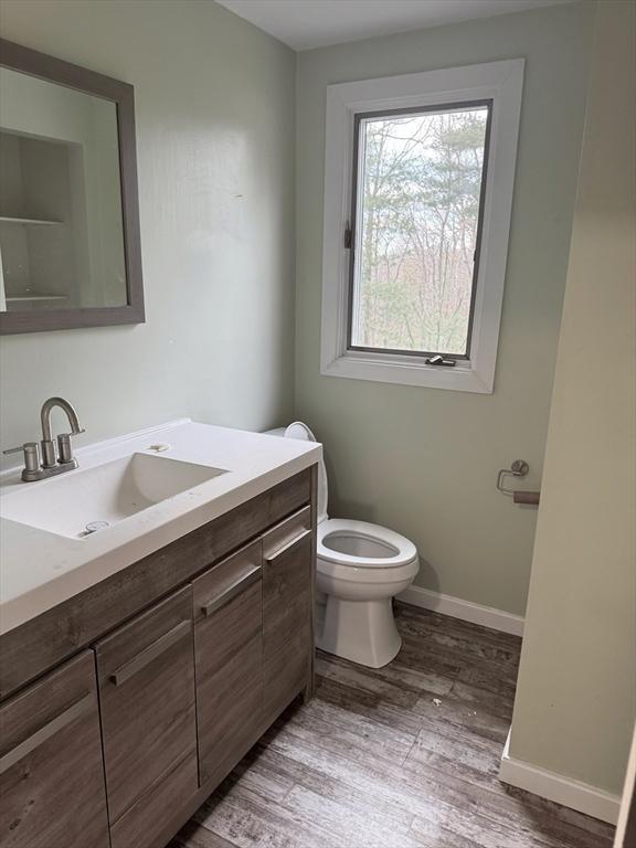 bathroom featuring toilet, baseboards, wood finished floors, and vanity