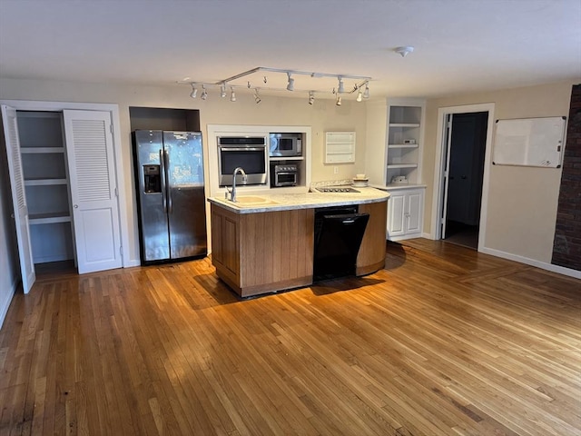 kitchen featuring baseboards, an island with sink, hardwood / wood-style flooring, black appliances, and a sink