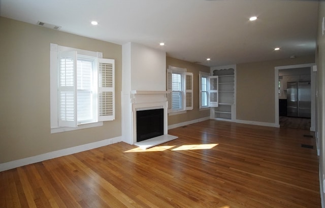 unfurnished living room featuring a healthy amount of sunlight, hardwood / wood-style floors, and built in features