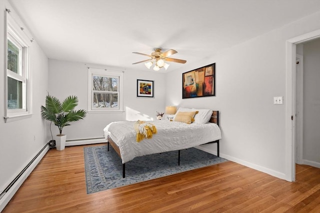 bedroom with a baseboard heating unit, light wood-type flooring, and baseboards