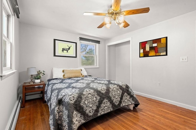 bedroom featuring a baseboard heating unit, a ceiling fan, baseboards, a closet, and dark wood-style floors