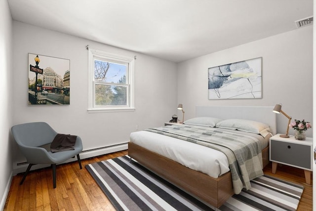 bedroom featuring a baseboard heating unit, wood finished floors, and visible vents