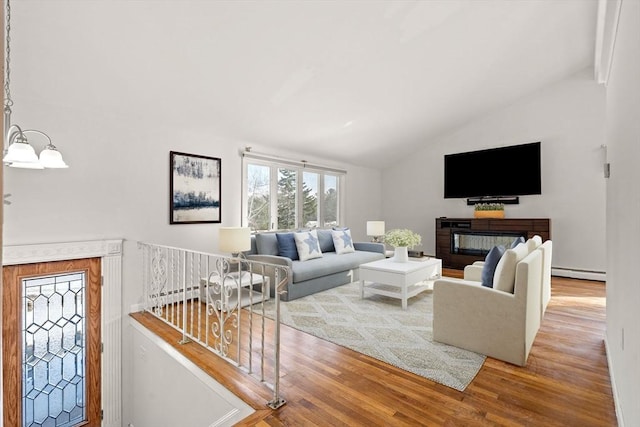 living room with a glass covered fireplace, lofted ceiling, wood finished floors, baseboard heating, and a notable chandelier