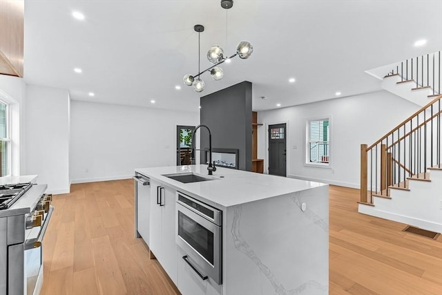 kitchen featuring stainless steel appliances, a sink, modern cabinets, hanging light fixtures, and an island with sink