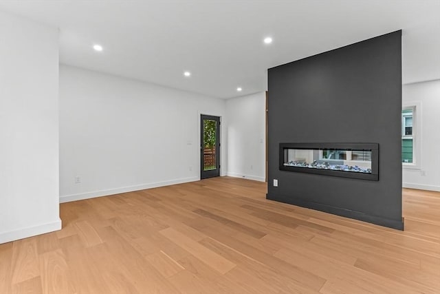 unfurnished living room featuring a multi sided fireplace, light wood-type flooring, recessed lighting, and baseboards
