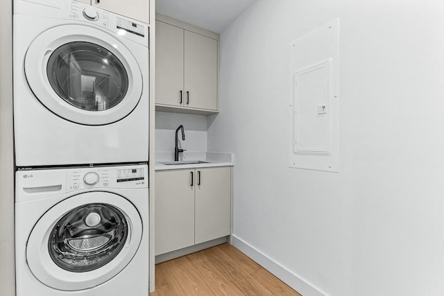 washroom with stacked washer / drying machine, cabinet space, electric panel, light wood-type flooring, and baseboards