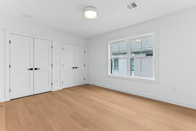 unfurnished bedroom with multiple closets, light wood-type flooring, and baseboards