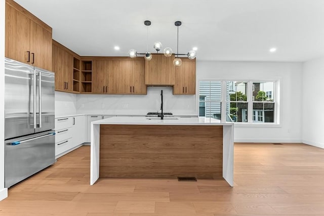 kitchen featuring high end refrigerator, open shelves, light countertops, light wood-type flooring, and hanging light fixtures