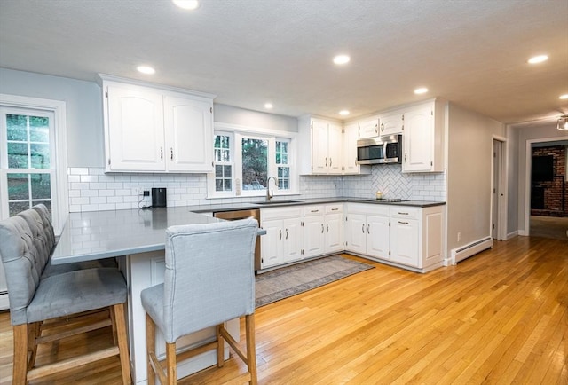 kitchen featuring white cabinetry, sink, baseboard heating, kitchen peninsula, and light hardwood / wood-style floors