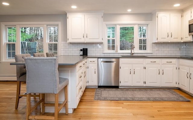 kitchen with appliances with stainless steel finishes, white cabinetry, baseboard heating, and sink