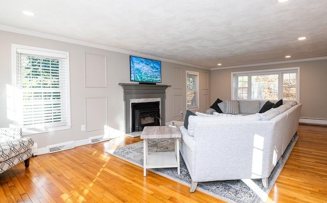 living room featuring baseboard heating, a high end fireplace, light hardwood / wood-style floors, and ornamental molding