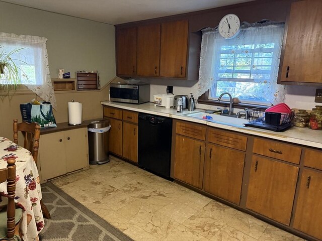 kitchen featuring stainless steel microwave, a sink, brown cabinetry, black dishwasher, and light countertops