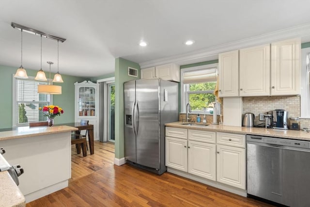 kitchen with stainless steel appliances, a sink, light wood-style flooring, white cabinets, and pendant lighting