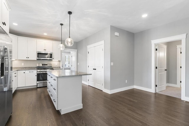 kitchen with light stone counters, stainless steel appliances, dark wood-type flooring, white cabinetry, and a kitchen island