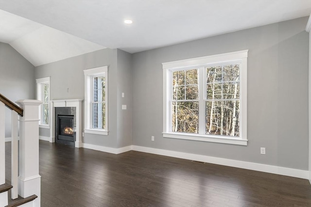 unfurnished living room with stairs, a glass covered fireplace, dark wood-style floors, and a healthy amount of sunlight