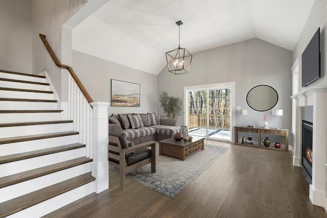 living area featuring high vaulted ceiling, wood finished floors, a lit fireplace, stairway, and an inviting chandelier