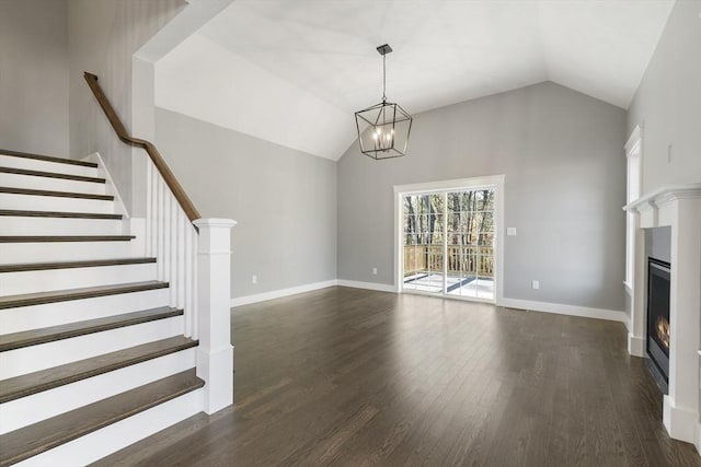 unfurnished living room with dark wood-style flooring, stairway, vaulted ceiling, a lit fireplace, and baseboards