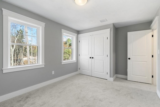 unfurnished bedroom with a closet, light carpet, and baseboards