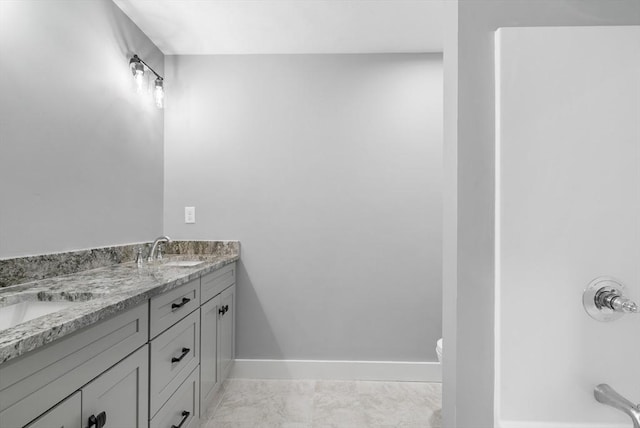 bathroom featuring marble finish floor, a sink, baseboards, and double vanity