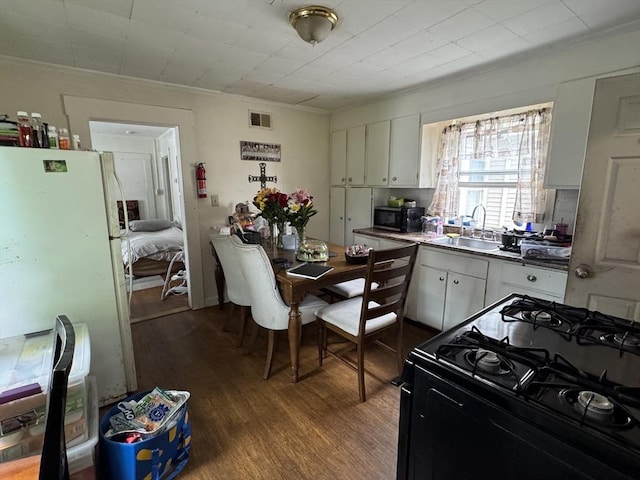 40 Freeman St, Framingham, MA 01702 - kitchen with black range with gas cooktop, freestanding refrigerator, white cabinetry, dark wood-type flooring, and crown molding