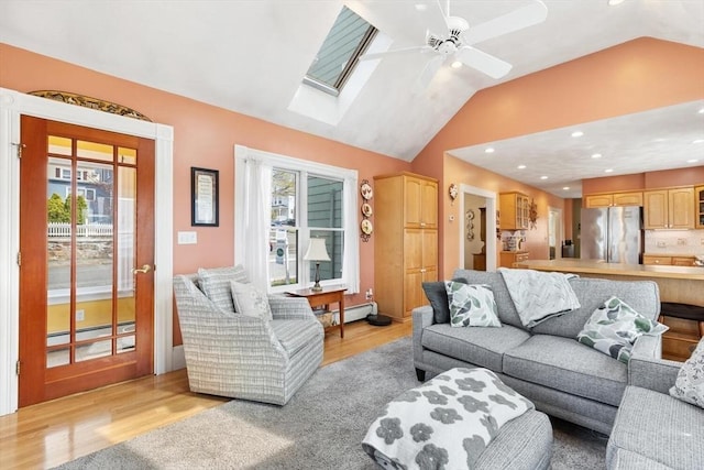 living room featuring vaulted ceiling with skylight, a ceiling fan, a baseboard radiator, recessed lighting, and light wood-style flooring