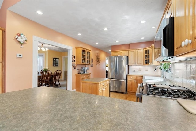 kitchen with backsplash, appliances with stainless steel finishes, a sink, a notable chandelier, and glass insert cabinets