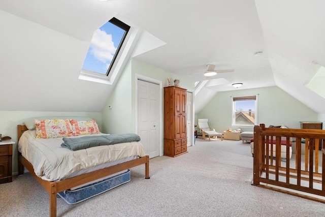bedroom featuring vaulted ceiling with skylight, ceiling fan, a closet, and light colored carpet