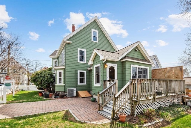 rear view of property featuring a deck, roof with shingles, a chimney, a patio area, and a yard