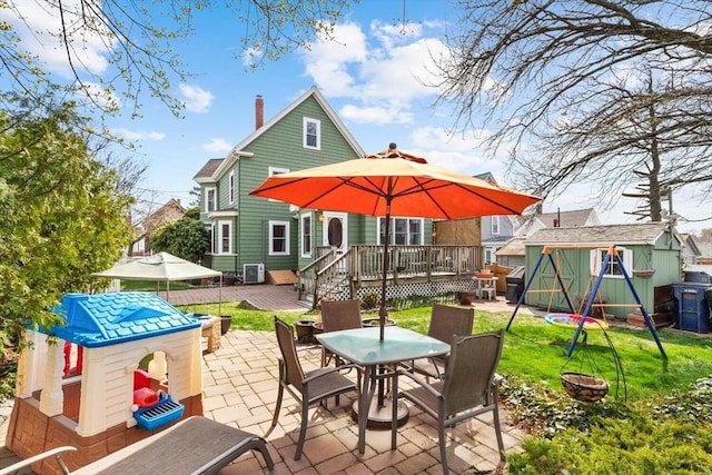 back of house with outdoor dining area, a storage shed, a wooden deck, an outdoor fire pit, and a patio
