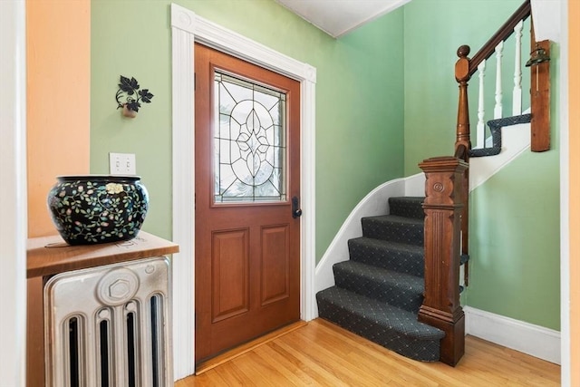 foyer featuring baseboards, radiator heating unit, stairway, and wood finished floors