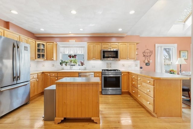 kitchen featuring a peninsula, a kitchen bar, tasteful backsplash, light wood finished floors, and appliances with stainless steel finishes