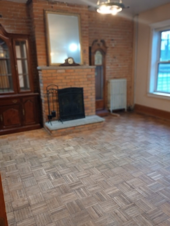 unfurnished living room featuring light parquet floors, a brick fireplace, and radiator