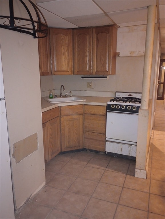 kitchen with light tile patterned floors, a drop ceiling, white gas stove, and sink