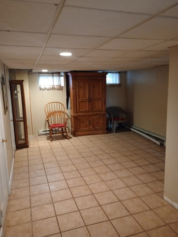 basement featuring a paneled ceiling, light tile patterned flooring, and a baseboard radiator