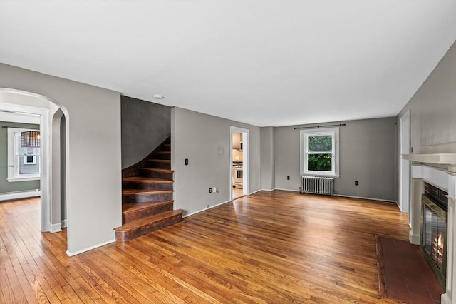7 Beaver St, Beverly, MA 01915 - unfurnished living room with radiator, hardwood / wood-style flooring, baseboard heating, a glass covered fireplace, and arched walkways