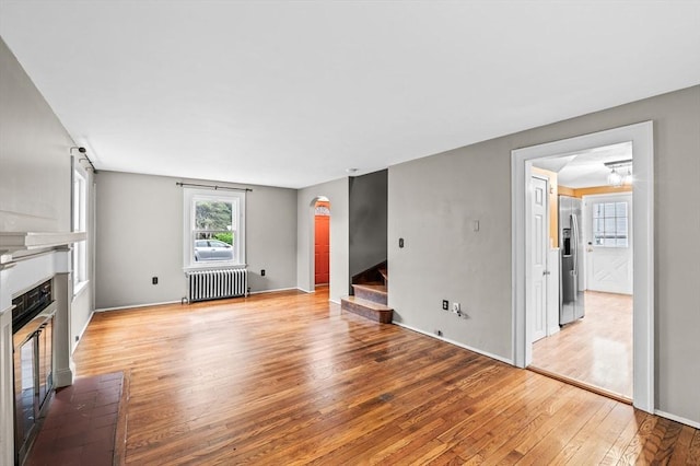 7 Beaver St, Beverly, MA 01915 - unfurnished living room featuring radiator, stairway, light wood-type flooring, a glass covered fireplace, and baseboards