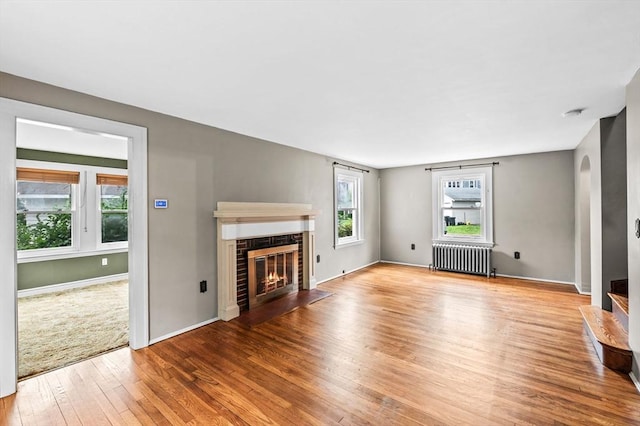 7 Beaver St, Beverly, MA 01915 - unfurnished living room featuring radiator heating unit, wood-type flooring, a fireplace with flush hearth, baseboards, and arched walkways