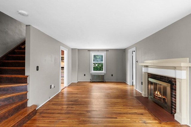 7 Beaver St, Beverly, MA 01915 - unfurnished living room with radiator heating unit, a brick fireplace, wood finished floors, and stairway