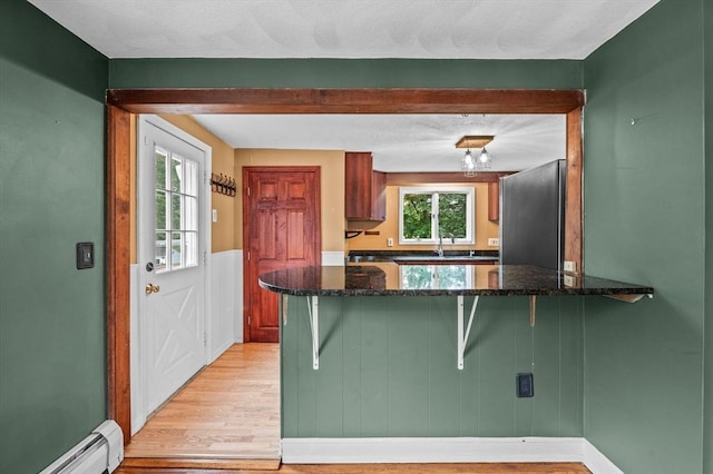 7 Beaver St, Beverly, MA 01915 - kitchen featuring a baseboard radiator, freestanding refrigerator, light wood-style flooring, a peninsula, and a kitchen bar