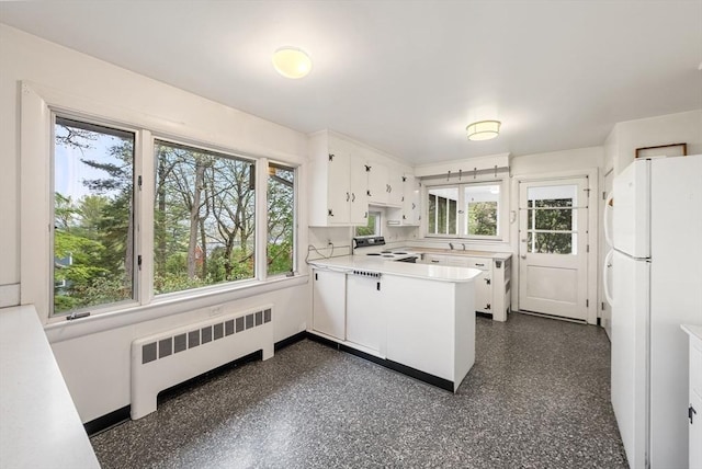 kitchen with radiator heating unit, freestanding refrigerator, a peninsula, and healthy amount of natural light