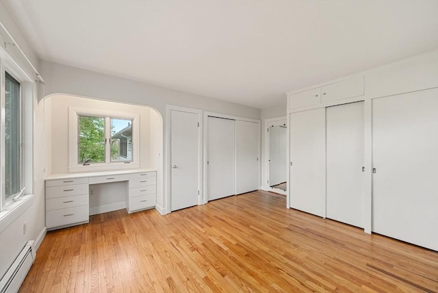 unfurnished bedroom featuring baseboard heating, light wood finished floors, and two closets